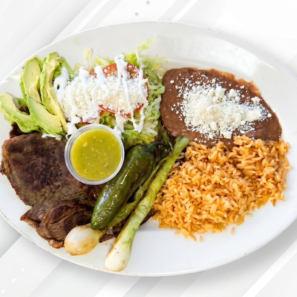 Carne asada plate with sliced avocado, salad, refried beans, rice, grilled peppers, and green onions.