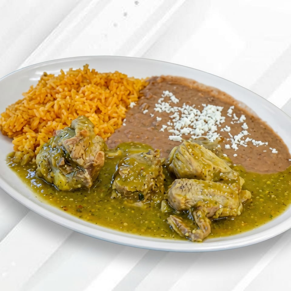 Pork in green chile sauce with rice and refried beans topped with cheese on a white plate.