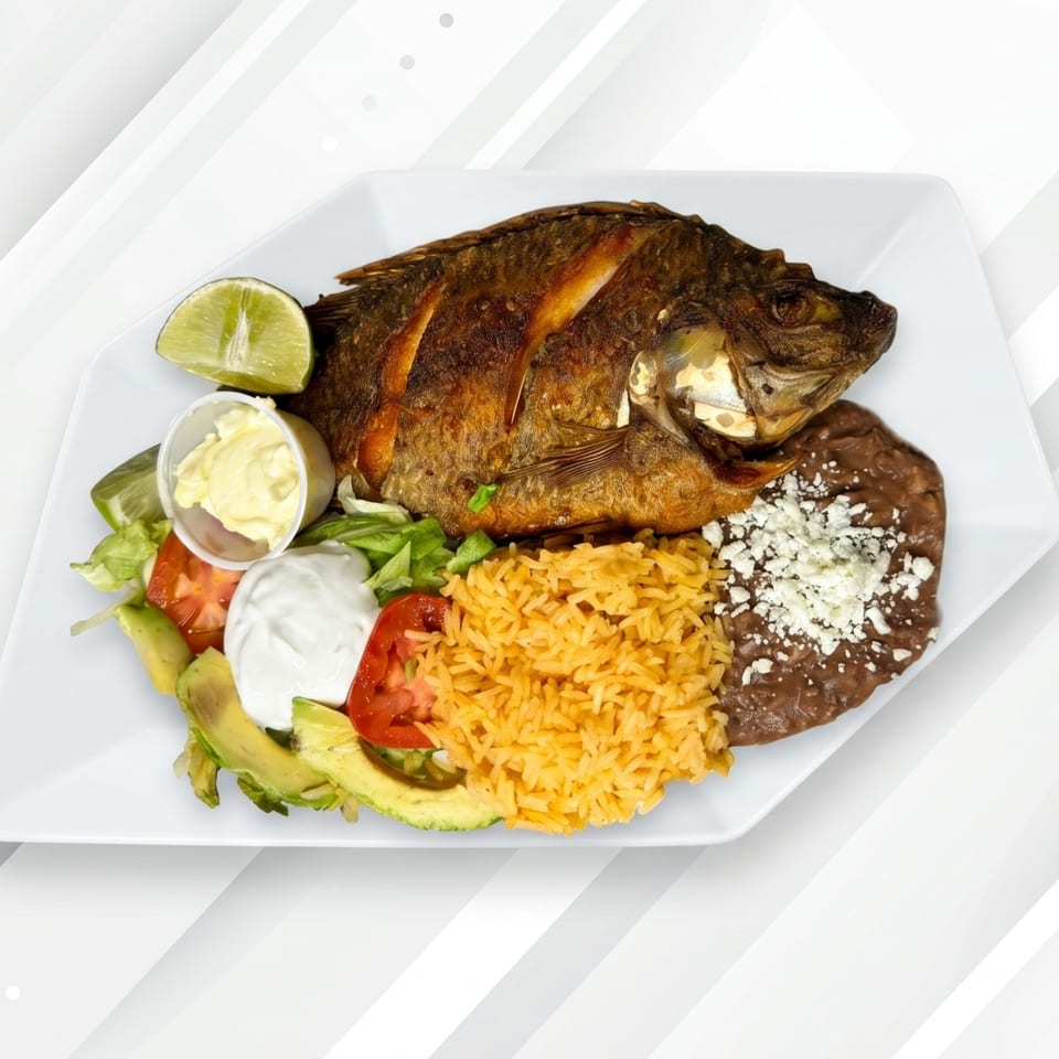 Whole fried fish with rice, refried beans, salad, avocado, and lime on a white plate.