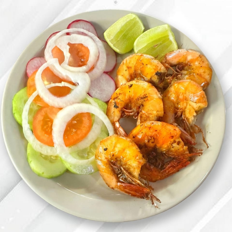 Plate of grilled shrimp with a side salad of sliced cucumbers, tomatoes, onions, radishes, and lime wedges.